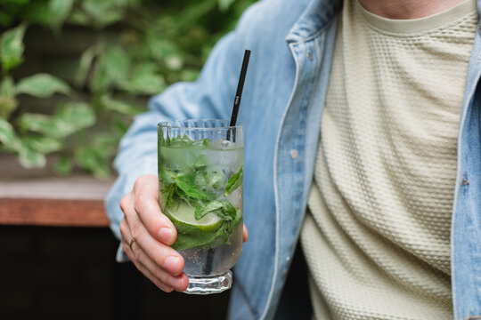 Close-up of a man standing at an outdoor cafe holding a refreshing drink with mint leaves and lime