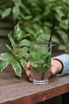 Close-up of a man sitting at an outdoor cafe holding a refreshing drink with mint leaves and lime