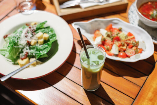 Close-up of an iced matcha latte, Caesar salad and tomato salad on garden table on a summer day