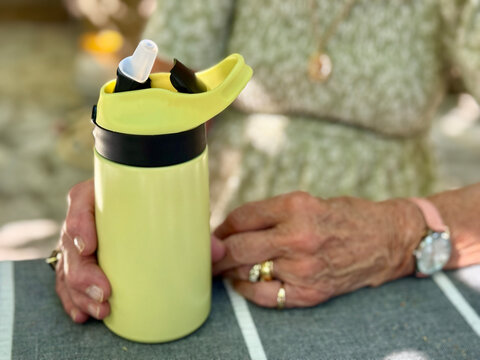 Close-up of a senior woman sitting at a table with a portable reusable water bottle on a summer day