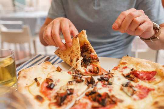 Close-up of a man sitting at an outdoor restaurant eating a slice of prosciutto ham and aubergine pizza