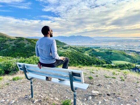 Rear view of a Hipster man Sitting on a Metal Bench at Sunset Point on the Wild Rose Loop Trail, North Salt Lake, Salt Lake City, Utah, USA