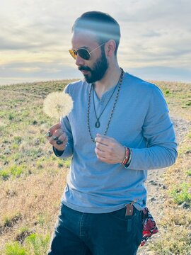 Hipster Man standing in a meadow holding a large dandelion clock on a summer day, Wild Rose Loop Trail, North Salt Lake, Salt Lake City, Utah, USA