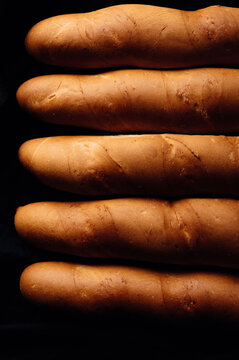 Close-up of five baguettes lined up in a row on a black background
