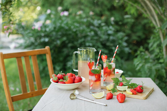 Close-up of a pitcher and two glasses of homemade strawberry lemonade with fresh mint on a garden table on a sunny summer day