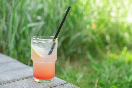 Close-up of a refreshing grapefruit lemonade with ice cubes on a garden ledge