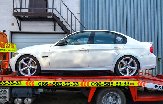 Profile side view of White modern BMW 3 Series E90 sedan loaded onto a flatbed tow truck. Features custom large alloy wheels and gold brake calipers