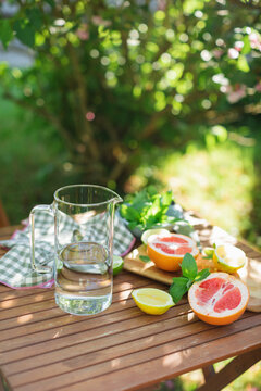 Close-up of a pitcher of water, mint leaves and assorted citrus fruit on a garden table in summer