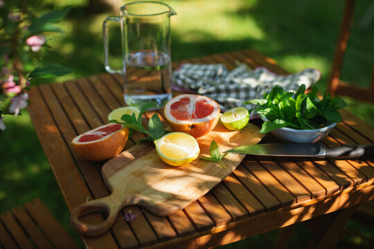 Close-up of a pitcher of water, mint leaves and assorted citrus fruit on a garden table in summer