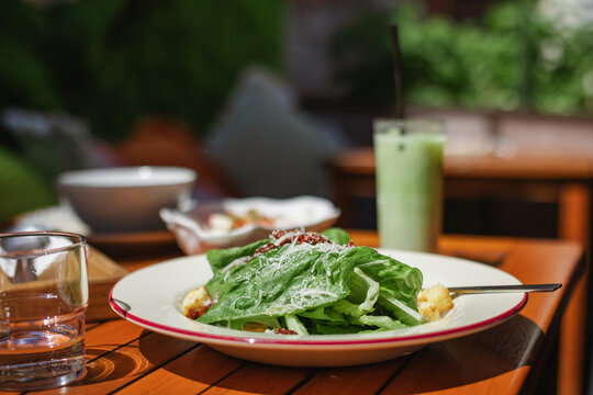 Close-up of a fresh Caesar salad with a glass of water and an iced matcha latte on a garden table on a summer day
