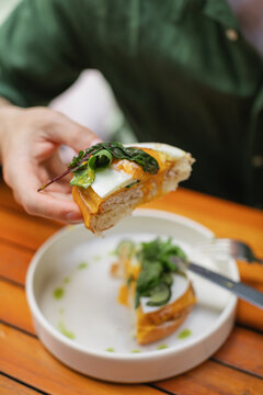 Close-up of a man sitting at a table eating a halved open-faced toasted egg and cheese bun