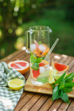 Close-up of a glass of water, mint leaves and assorted citrus fruit on a garden with a pitcher and napkin on a table in summer