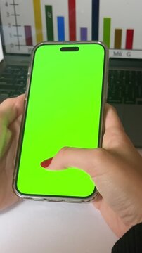 Young woman's hand holding mobile phone with green screen in her office desk.Modern and realistic 4k video.Perfect for agencies and content creators