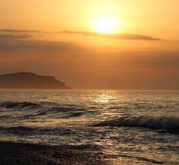 Obraz premium Peaceful beach at sunset featuring gentle ocean waves, golden light, and a colorful evening sky.