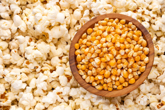 Popcorn kernels in a wooden container surrounded by popcorn, perfect for movie, snack, cooking, and food themes