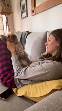 Young woman pampering her dog on the couch, natural light coming through the window, scene of affection and emotional bond between human and pet.Vertical 4k video