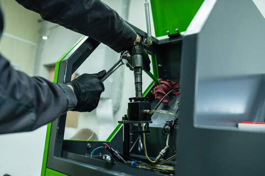 Mechanic hand in glove tightening diesel fuel injector with wrench tool on test bench for calibration in repair workshop