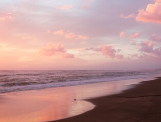Obraz premium Peaceful beach at sunset featuring gentle ocean waves, golden light, and a colorful evening sky.