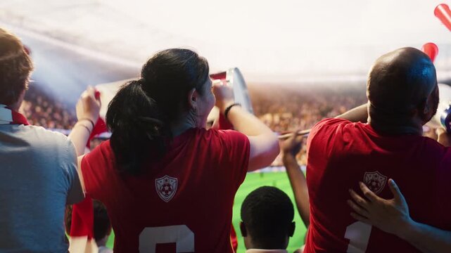 Supporters in red soccer kits blowing vuvuzelas during match day in packed stadium, showing cheering crowd creates passionate fan chants with air horns to show team support for fan culture content.
