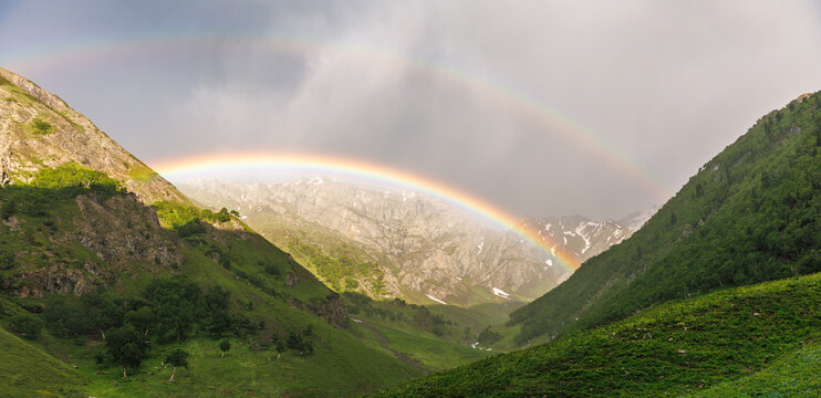 A double rainbow forms a majestic glowing gateway over a dramatic mountain pass in the Himalayas, Natural gateway framed by vivid green slopes and a rare double rainbow in Gilgit Baltistan, 