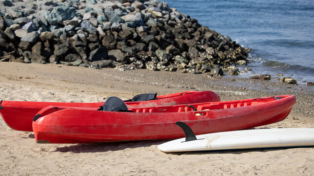 Two red kayaks and a paddle board by the shore. Water activities equipment.