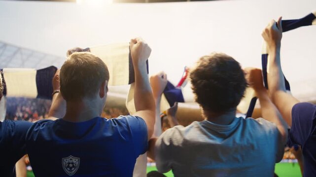 Close up of football supporters in team jerseys raising hands with scarves during soccer match day in packed stadium for fan culture and team support content.