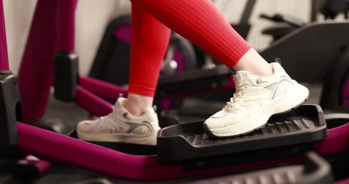 Strong woman training on elliptical machine in gym, closeup
