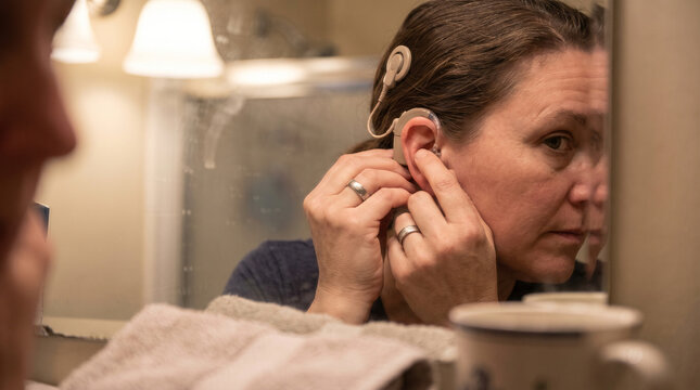 Middle aged woman fitting cochlear device in ear
