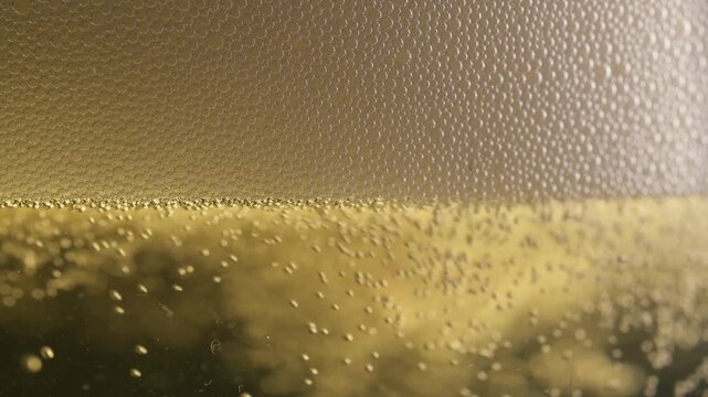 Macro close up of golden beer being poured with rising foam and sparkling bubbles creating refreshing lager background