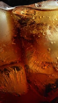 Macro close up of sparkling cola soda with ice cubes and rising bubbles creating refreshing cold soft drink background