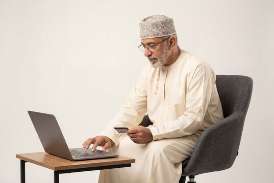 Senior omani man in traditional dress using a laptop and holding a credit card