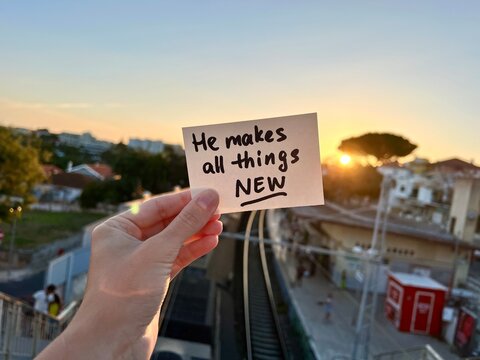He makes all things new - hand with christian text sunset outdoors, biblical motivation card