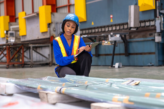Female factory worker inspecting quality rolls of galvanized or metal sheet in factory. Hispanic female worker working in warehouse of raw materials in metal manufacturing factory.