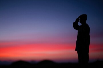 Fototapeta premium Dramatic sunset sky background with soldier silhouette saluting on a hilltop for Veterans Day, Memorial Day and patriotic military tribute advertising with copy space