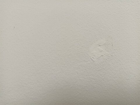 Close‑up view of a white textured wall with a small patched area showing fresh filler or spackling compound.