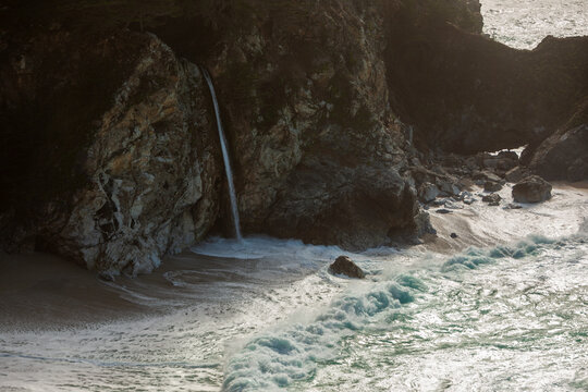 McWay Falls cascades onto a sandy beach in Julia Pfeiffer Burns State Park, Big Sur, California, USA. The powerful ocean waves crash against the rocky shore.