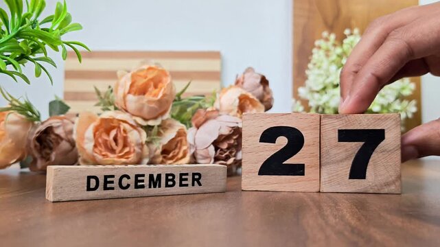 Hand placing wooden calendar blocks showing december 27 on a wooden table