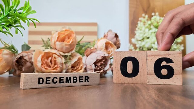 Hand placing wooden calendar blocks showing december 6 on a wooden table