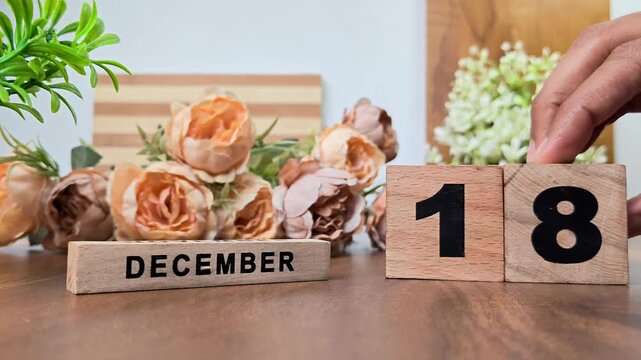 Hand placing wooden calendar blocks showing december 18 on a wooden table