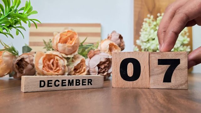 Hand placing wooden calendar blocks showing december 7 on a wooden table