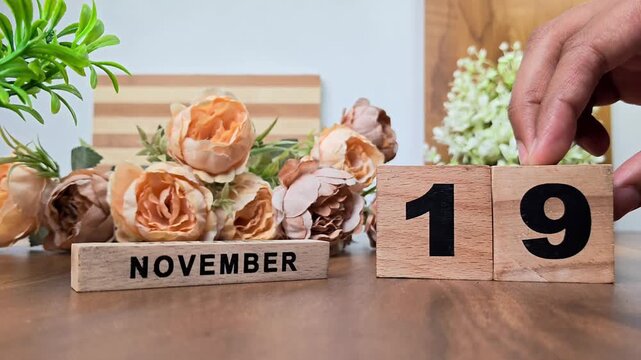 Hand placing wooden calendar blocks showing november 19 on a wooden table