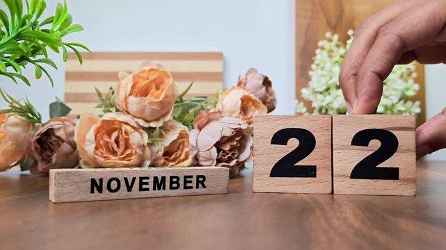 Hand placing wooden calendar blocks showing november 22 on a wooden table