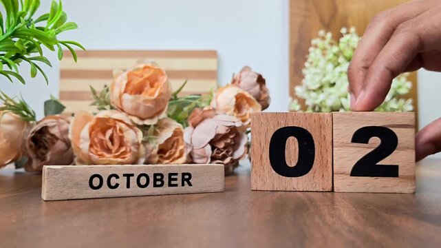 Hand placing wooden calendar blocks showing october 2 on a wooden table