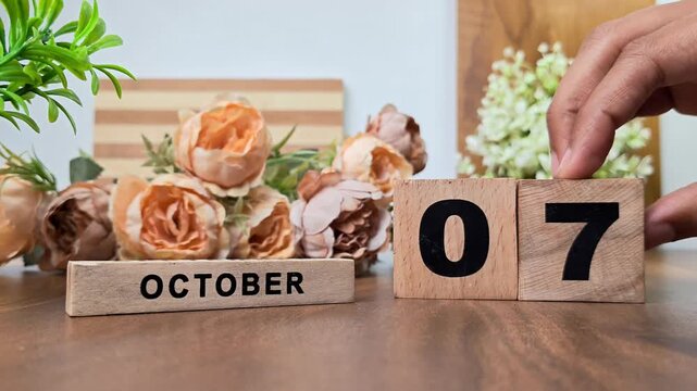 Hand placing wooden calendar blocks showing october 7 on a wooden table