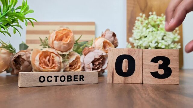 Hand placing wooden calendar blocks showing october 3 on a wooden table
