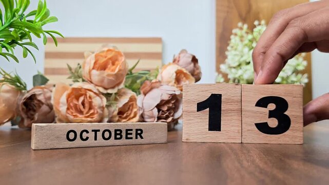 Hand placing wooden calendar blocks showing october 13 on a wooden table