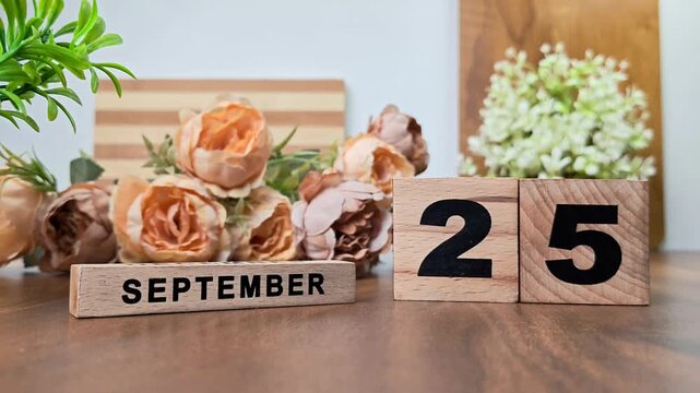 Hand placing wooden calendar blocks showing september 25 on a wooden table