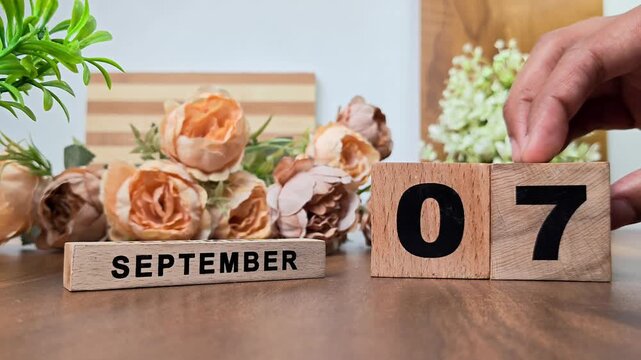 Hand placing wooden calendar blocks showing september 7 on a wooden table