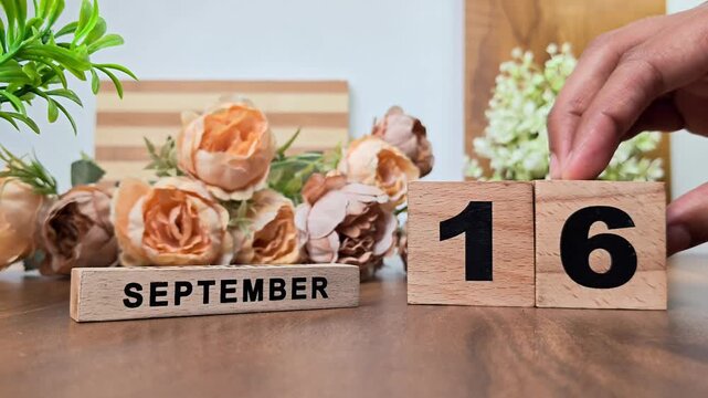 Hand placing wooden calendar blocks showing september 16 on a wooden table