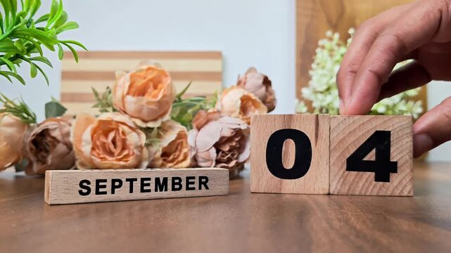 Hand placing wooden calendar blocks showing september 4 on a wooden table